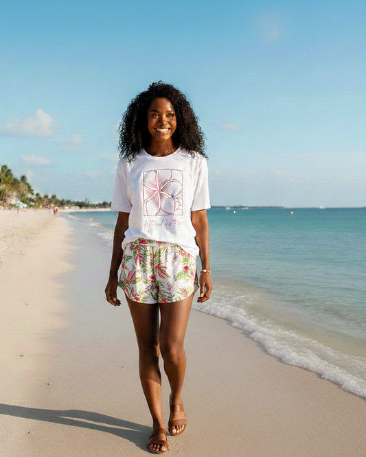 Woman standing on a beach wearing a white t-shirt with a graphic design and floral shorts. Bracelet on her wrist.