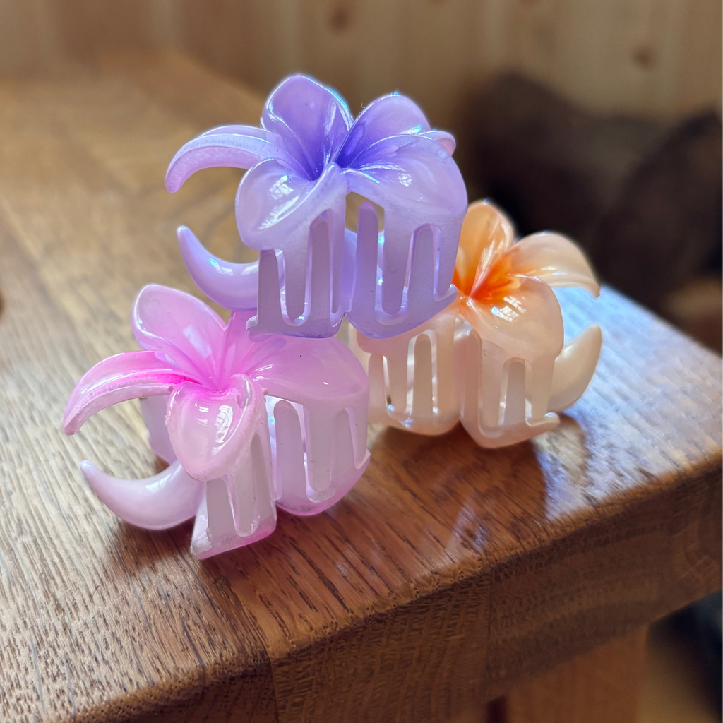 Three floral-shaped hair clips in pink, purple, and orange on a wooden surface.