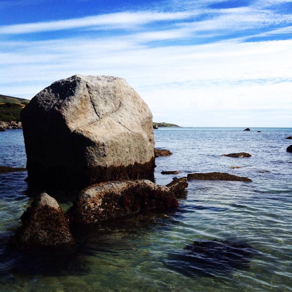 Large rock in shallow water with a clear blue sky above