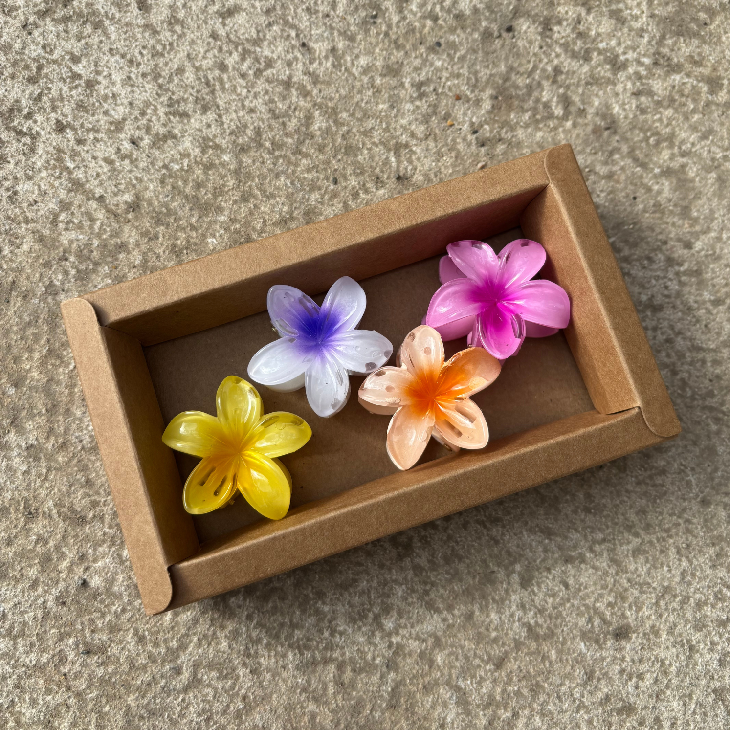 Colourful flower-shaped hair clips in a cardboard box on a stone surface