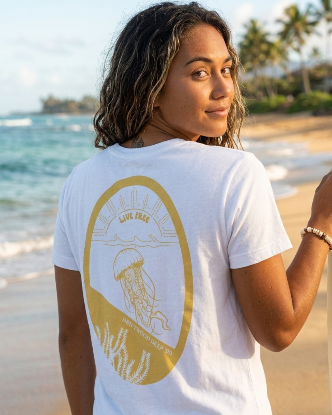 Person wearing a white t-shirt with a gold graphic on the beach