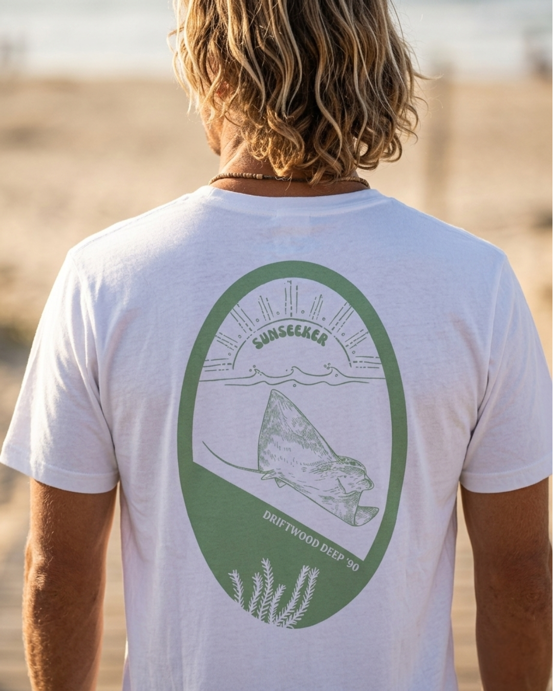 Person wearing a white t-shirt with a green graphic on the beach