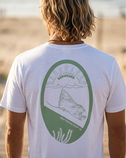 Person wearing a white t-shirt with a green graphic on the beach