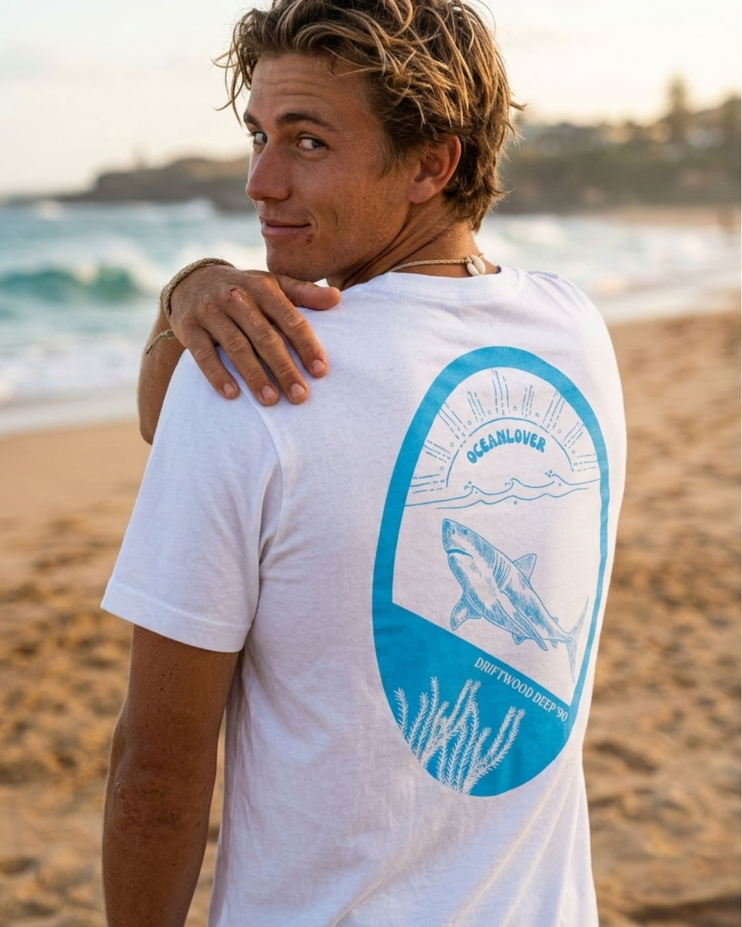 Person wearing a white t-shirt with a shark graphic on the beach