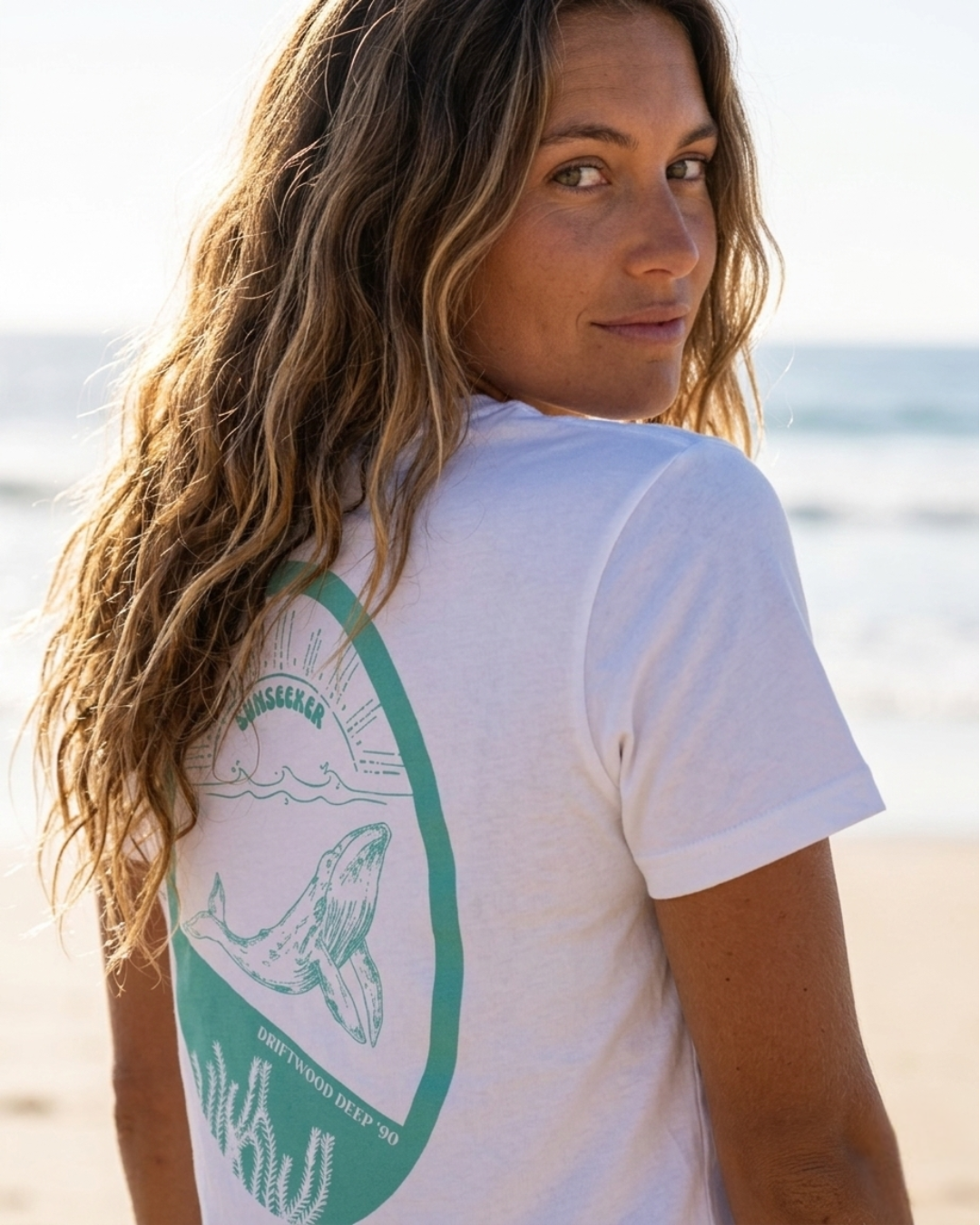 Woman wearing a white t-shirt with a green graphic on the beach