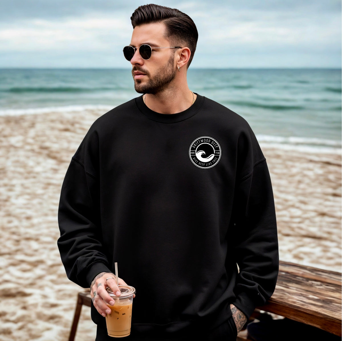 Man wearing a black sweatshirt with a logo on a beach