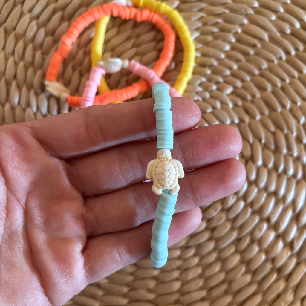 Hand holding a turquoise bracelet with a turtle charm against a woven background