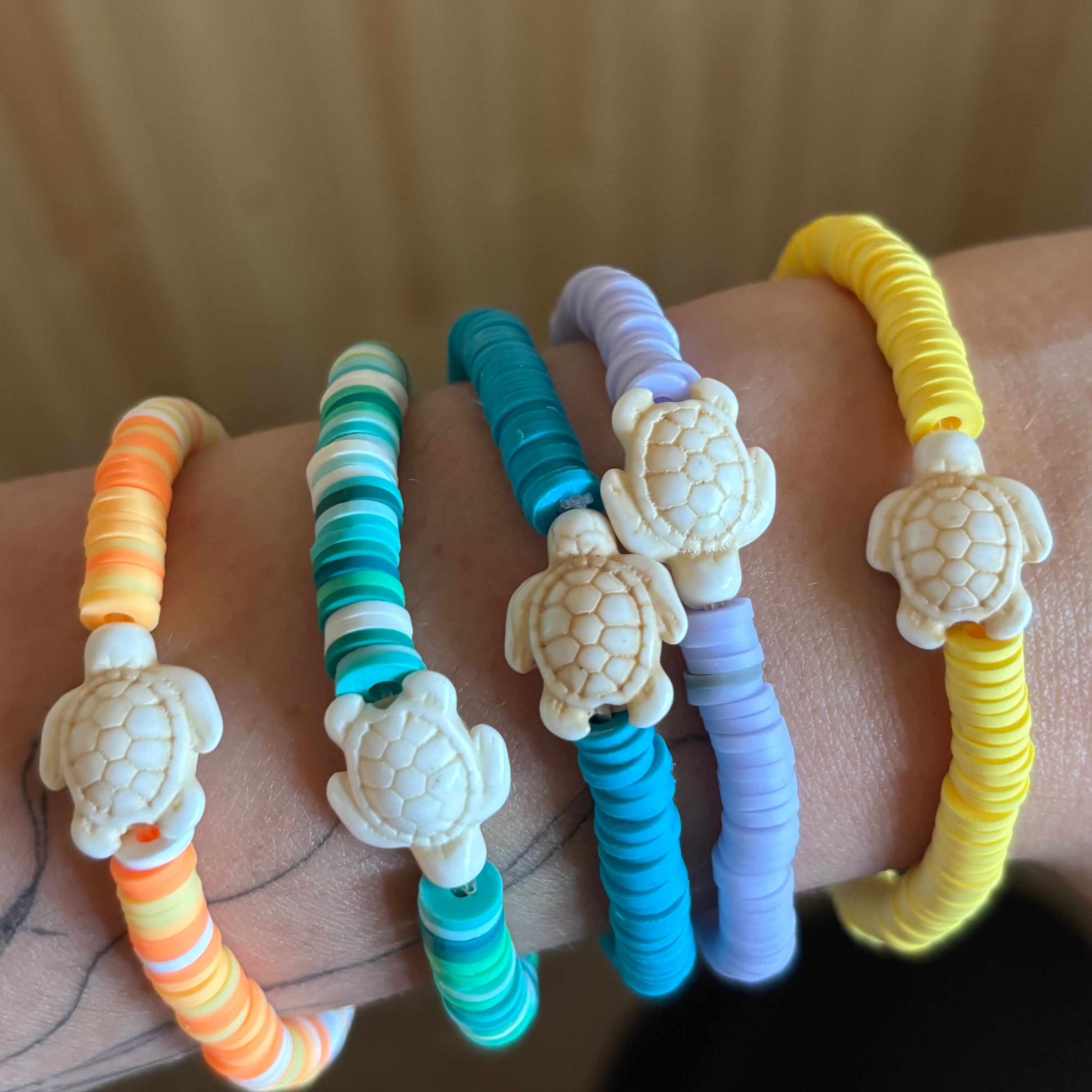Colourful bracelets with turtle charms on a wrist against a wooden background