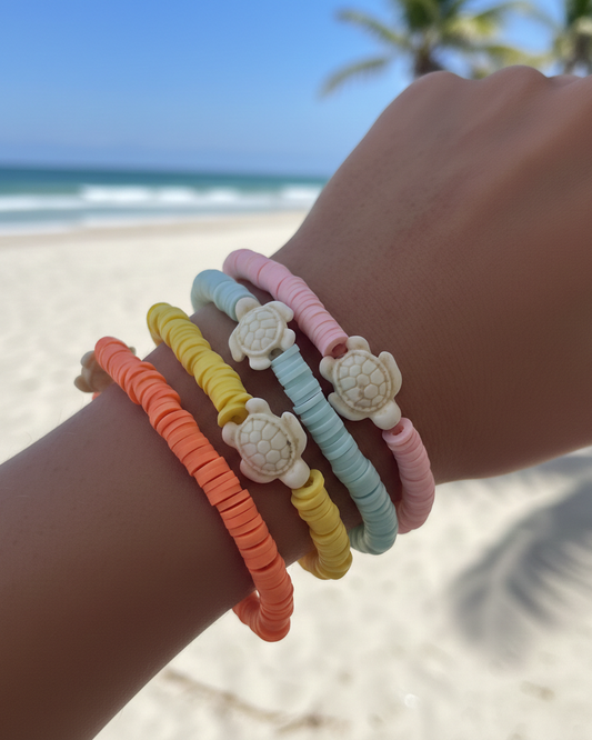 Colourful turtle-themed bracelets on a wrist with a beach background