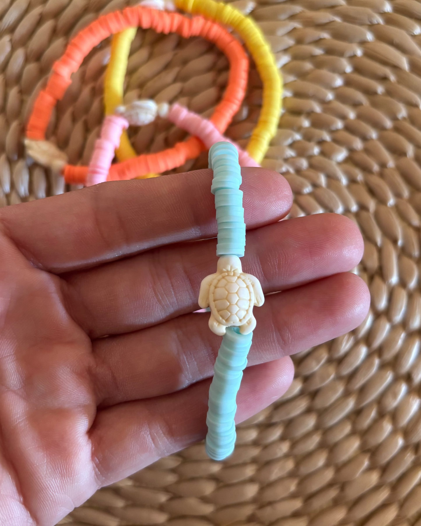 Hand holding a turquoise bracelet with a turtle charm against a woven background