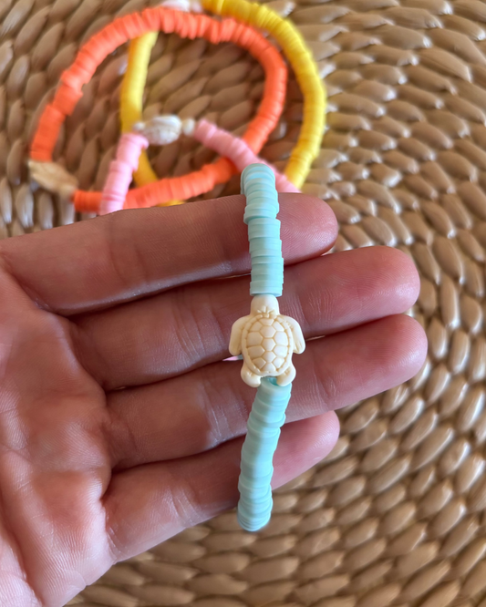 Hand holding a turquoise bracelet with a turtle charm against a woven background