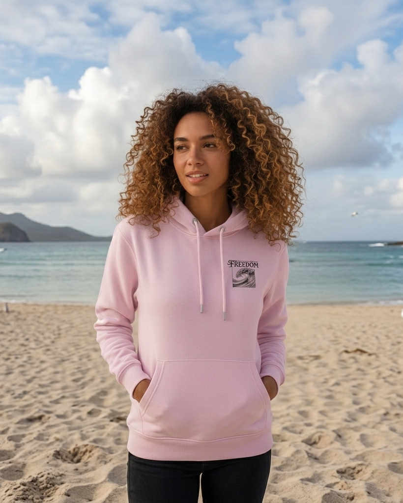 Woman wearing a pink hoodie on a beach with ocean and sky in the background