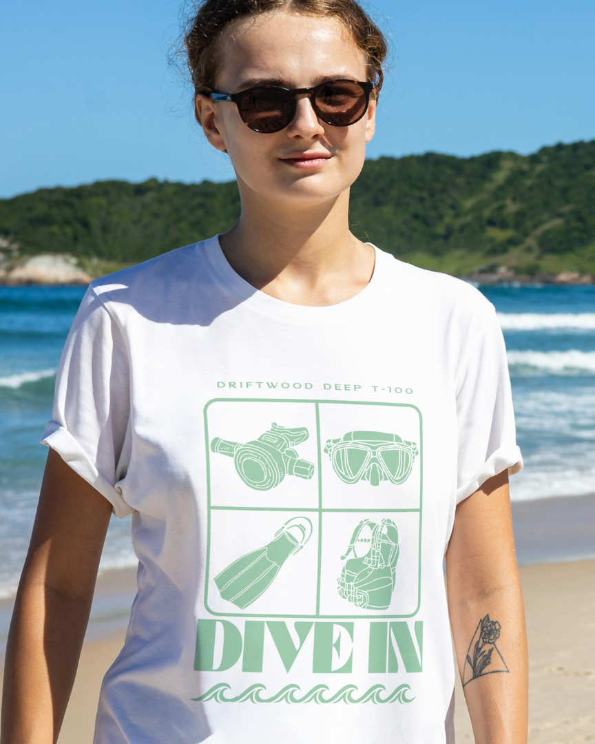 Woman wearing a white t-shirt with green graphics and text on a beach.