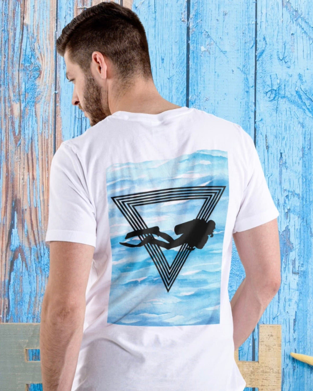 Man wearing a white t-shirt with a scuba diving design on the back against a blue wooden background