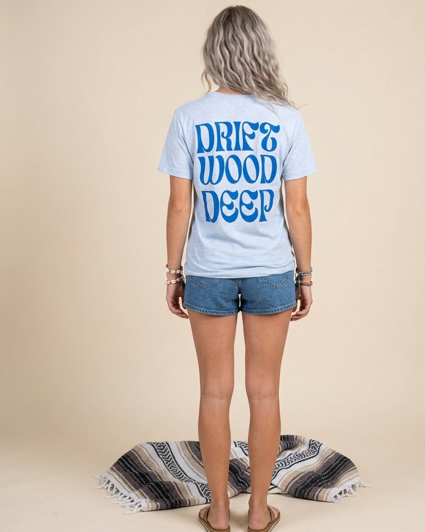 Person wearing a light blue t-shirt with 'DRIFT WOOD DEEP' text on the back, standing against a beige background.