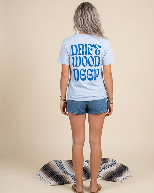 Person wearing a light blue t-shirt with 'DRIFT WOOD DEEP' text on the back, standing against a beige background.