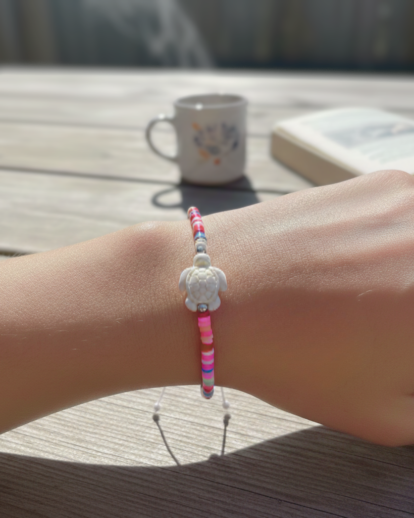 Bracelet with pink and white design on wrist, blurred background with cup and book
