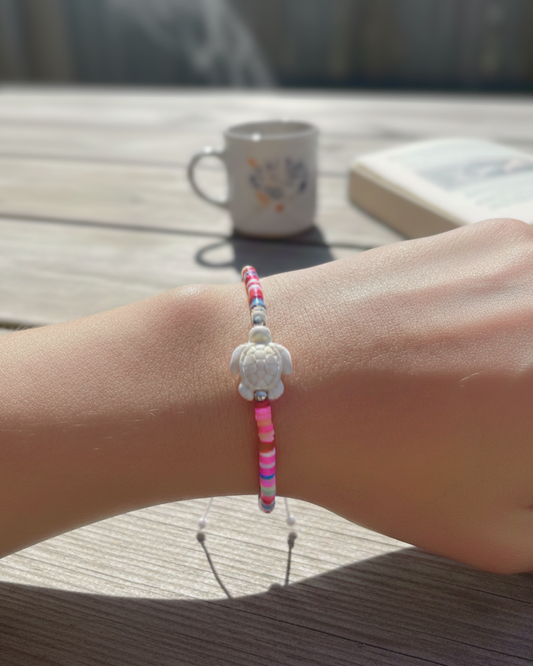 Bracelet with pink and white design on wrist, blurred background with cup and book
