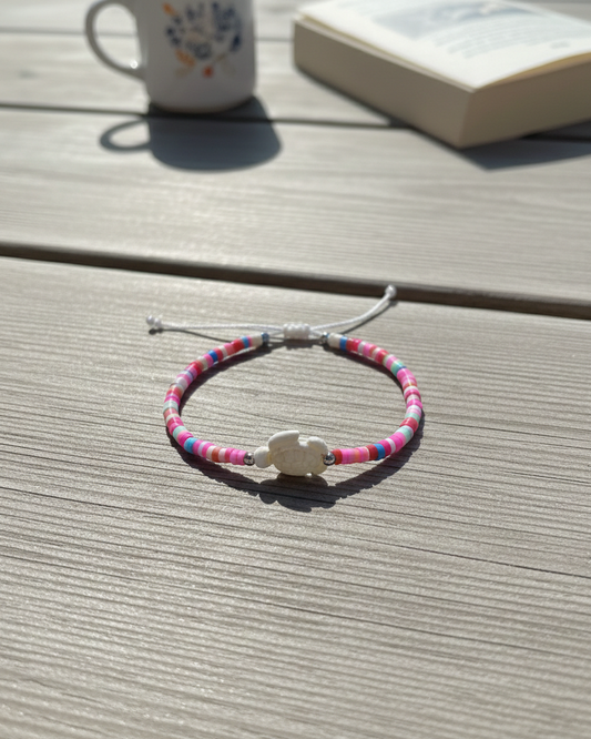 Bracelet with colorful beads and a silver clasp on a wooden surface, with a mug and book in the background.