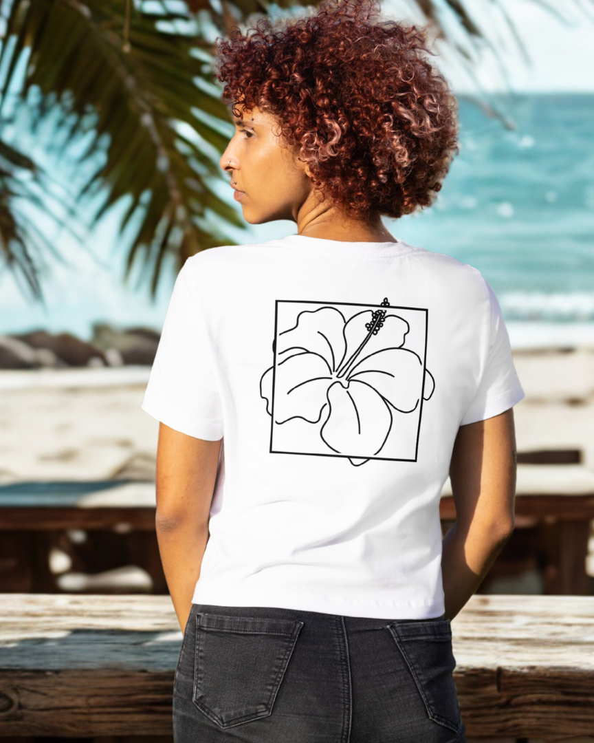 Person wearing a white t-shirt with a black floral design on the back, standing by the ocean.