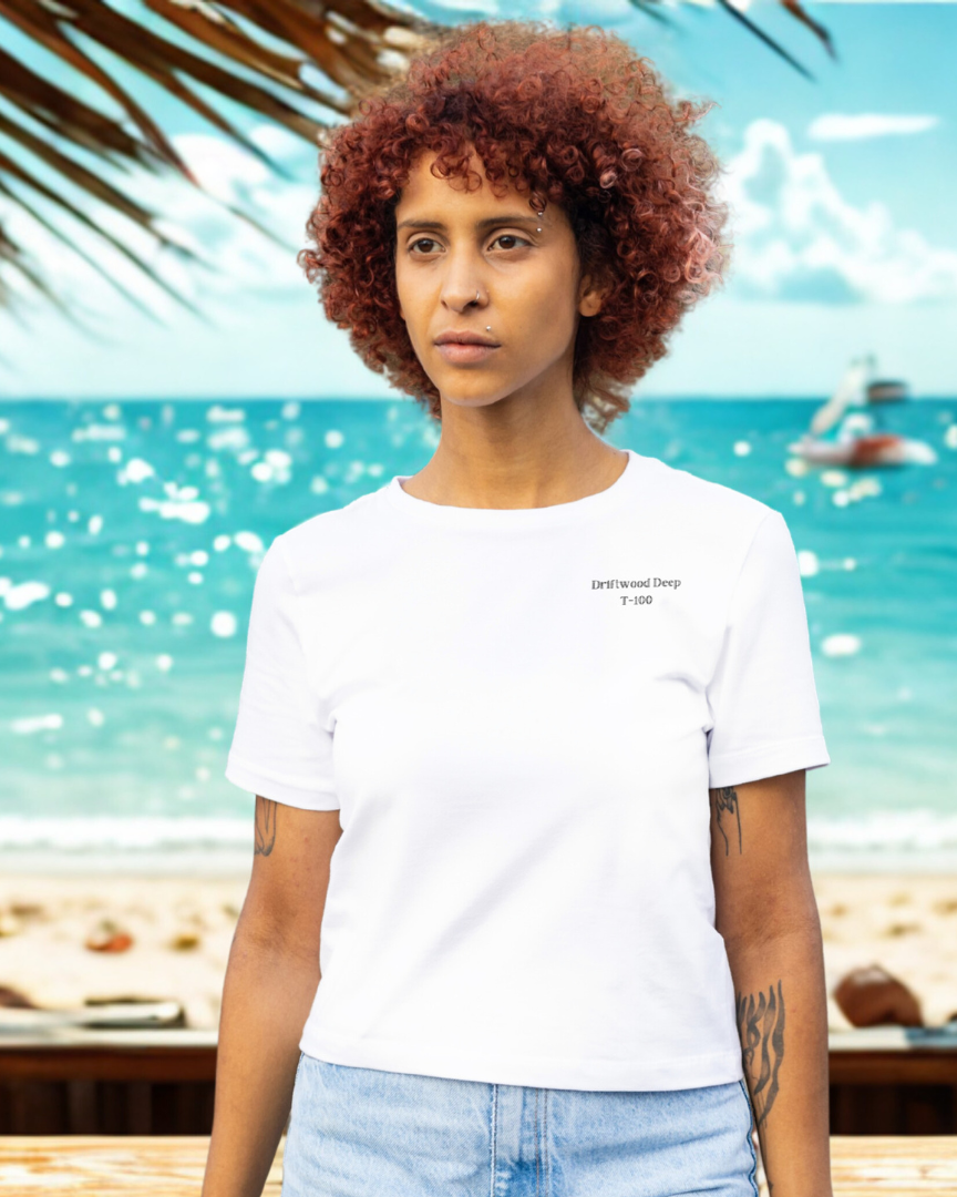 Person wearing a white t-shirt and light blue jeans standing on a beach with ocean and sky in the background.