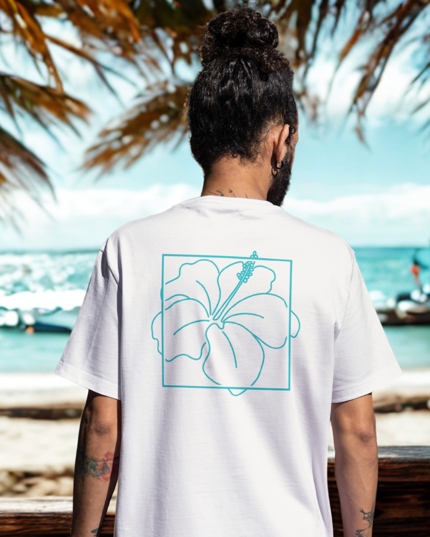 Person wearing a white t-shirt with a blue floral design on the back, standing by a beach with palm trees and water in the background.