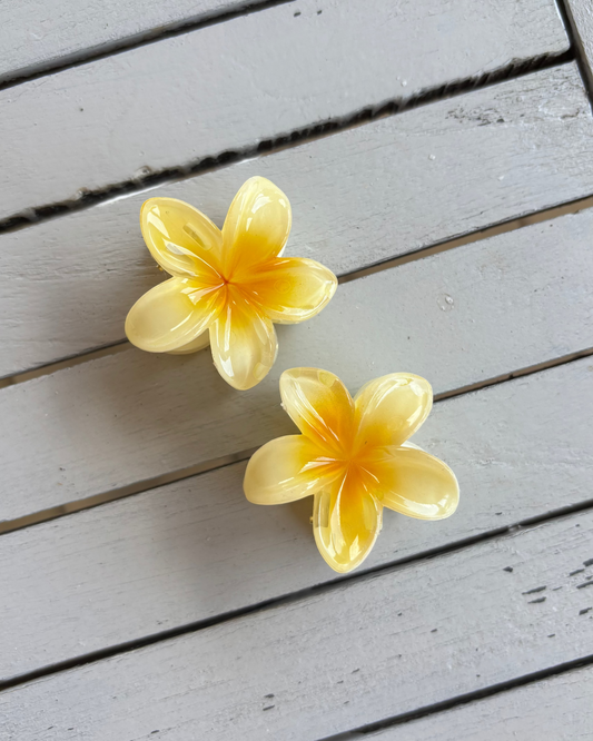 Two yellow flower-shaped hair clips on a wooden surface