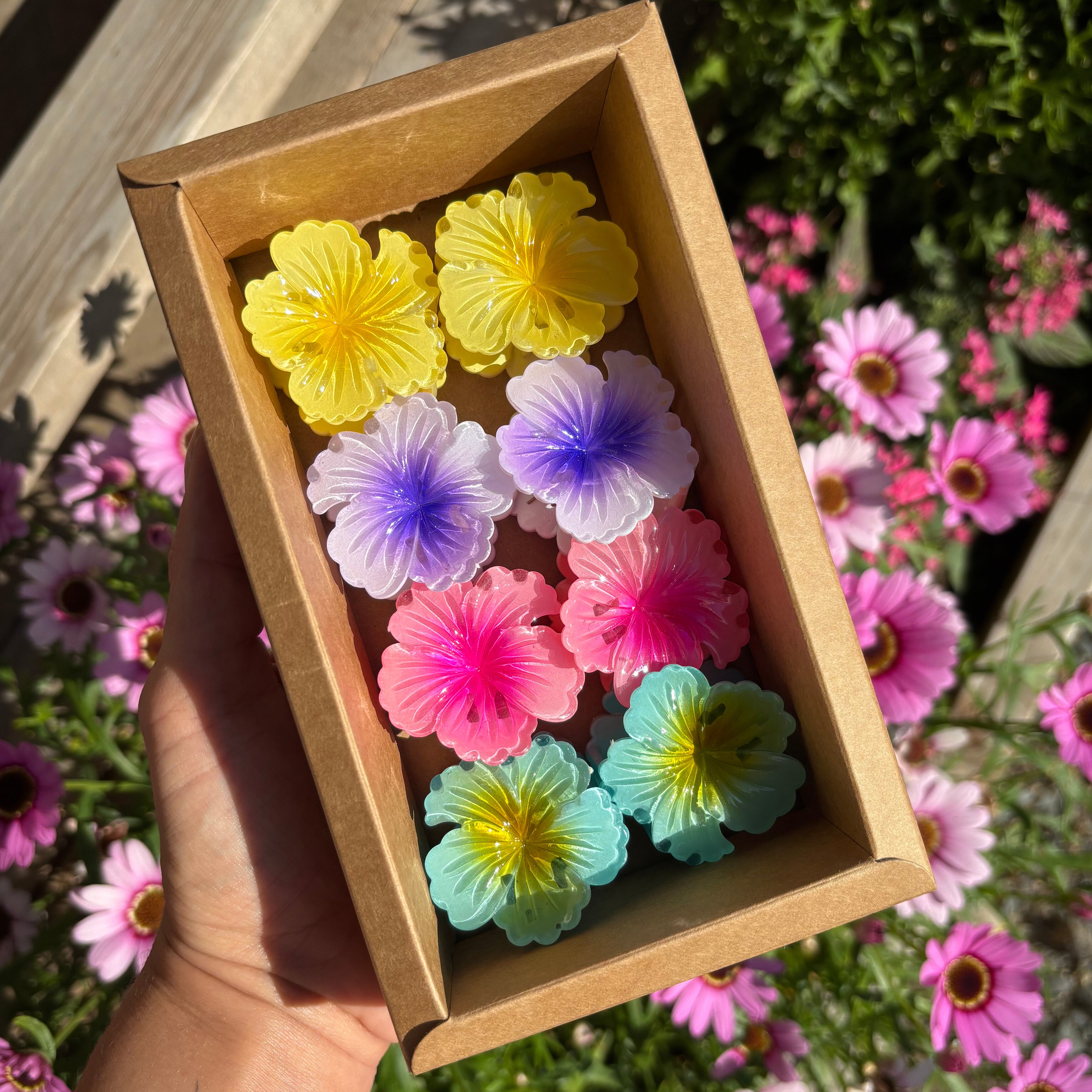 Box of colourful flower-shaped hair clips held in front of a garden with flowers.