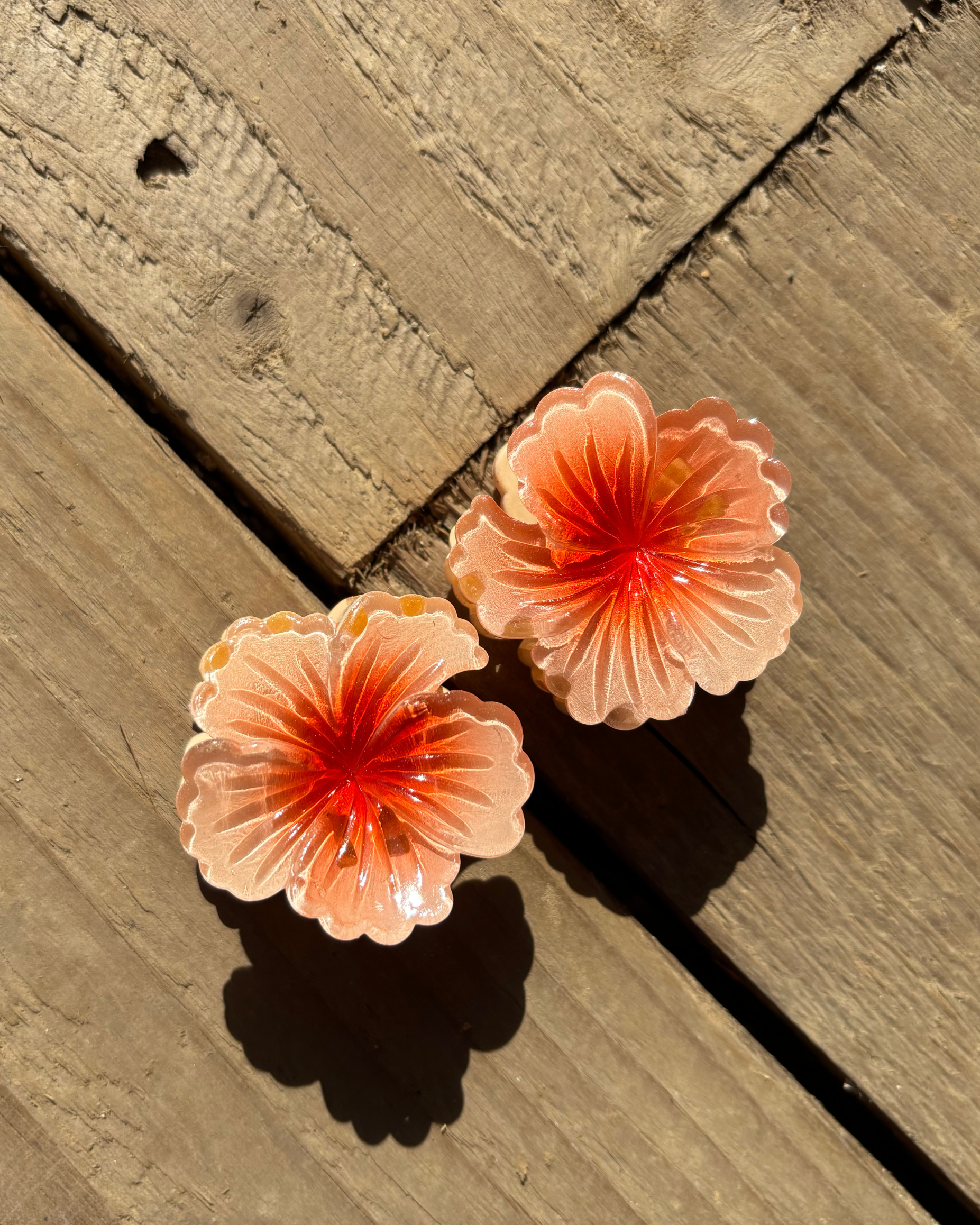 Two peach-colored flower-shaped hair clips on a wooden surface