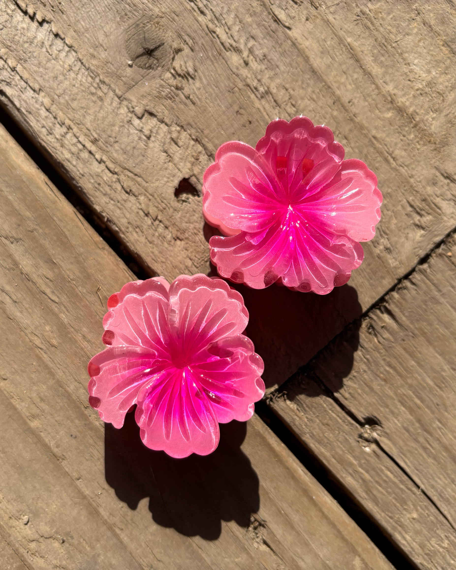 Two pink flower-shaped hair clips on a wooden surface