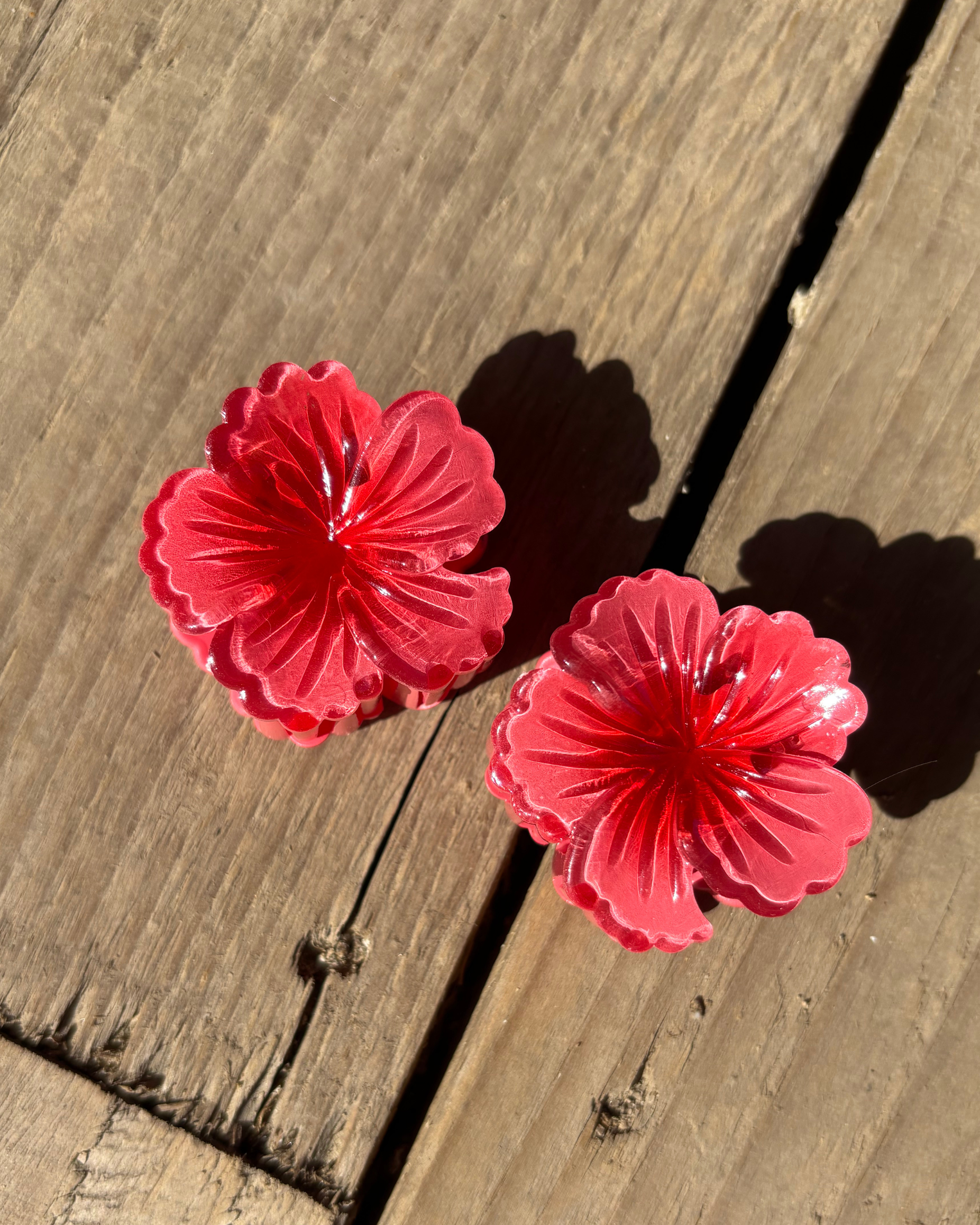 Two red flower-shaped hair clips on a wooden surface
