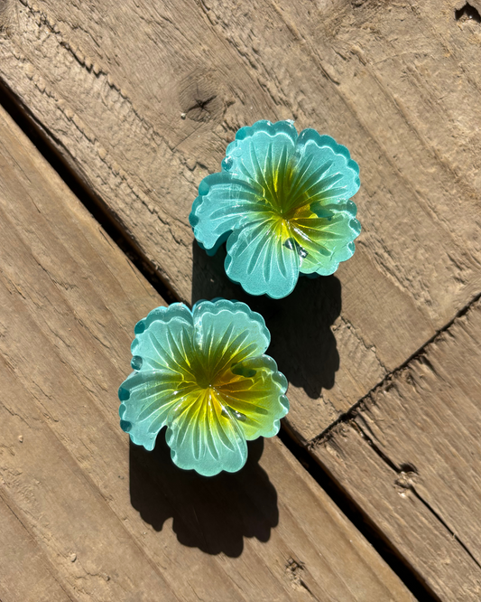 Two turquoise flower-shaped hair clips on a wooden surface