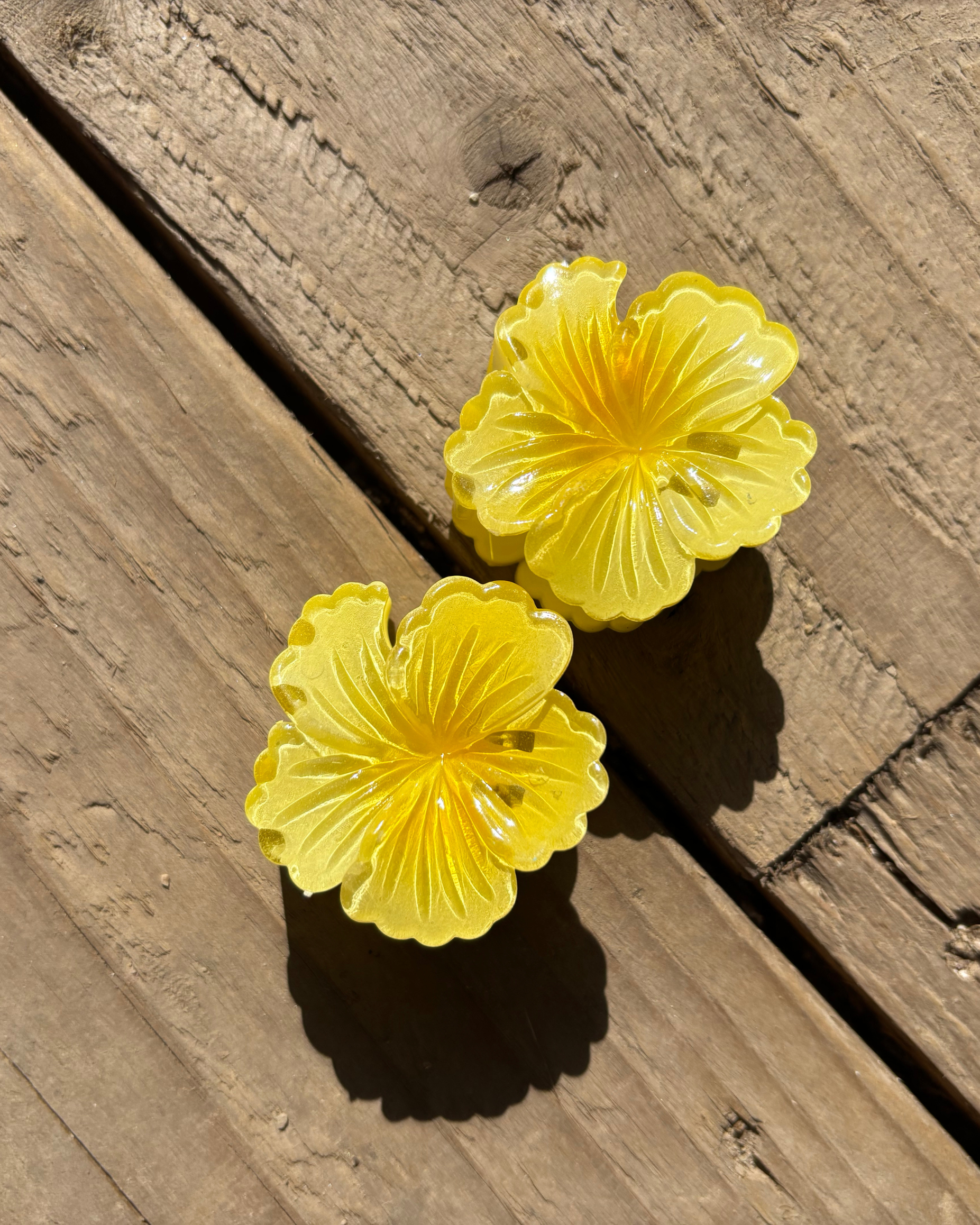 Two yellow flower-shaped hair clips on a wooden surface