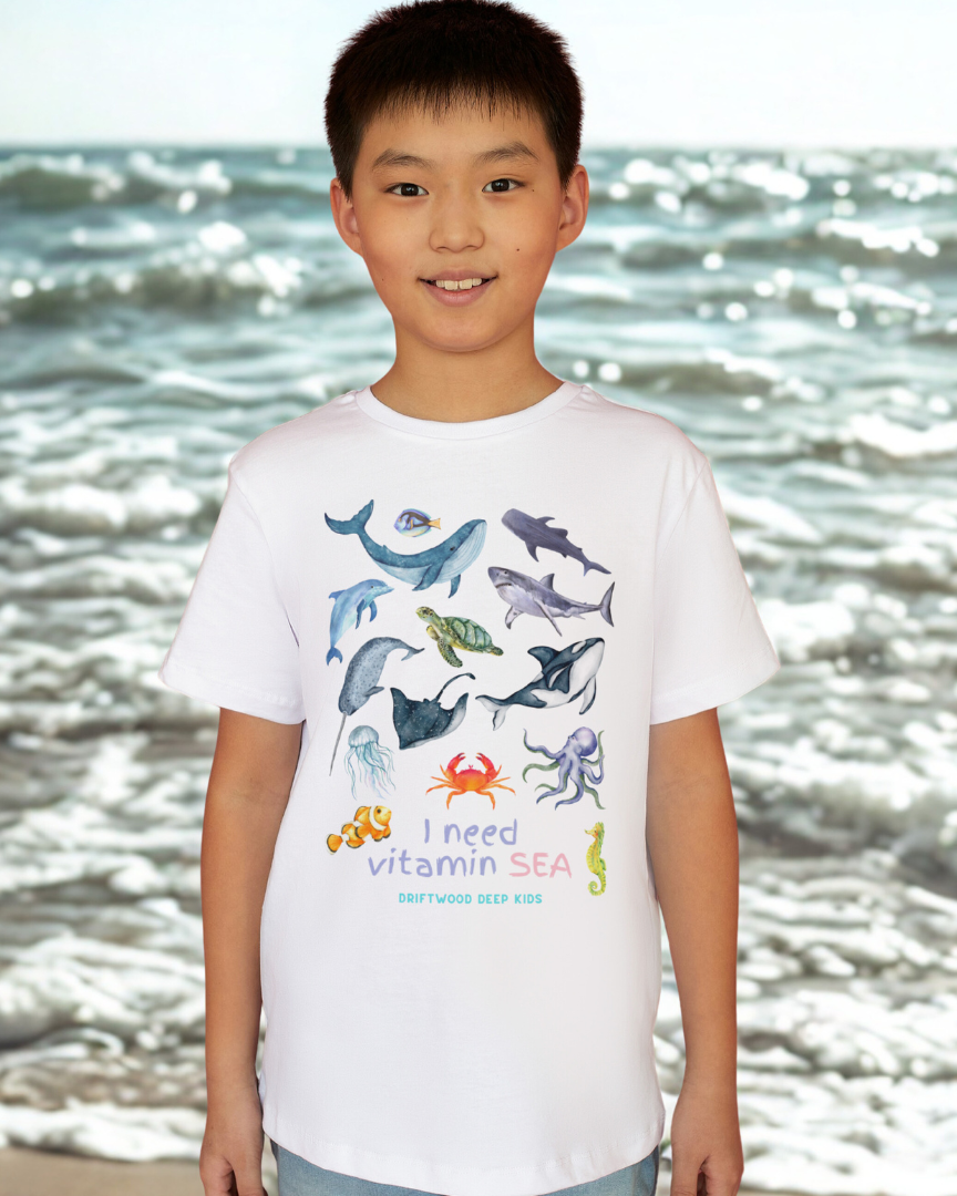 Child wearing a t-shirt with sea-themed designs on a beach