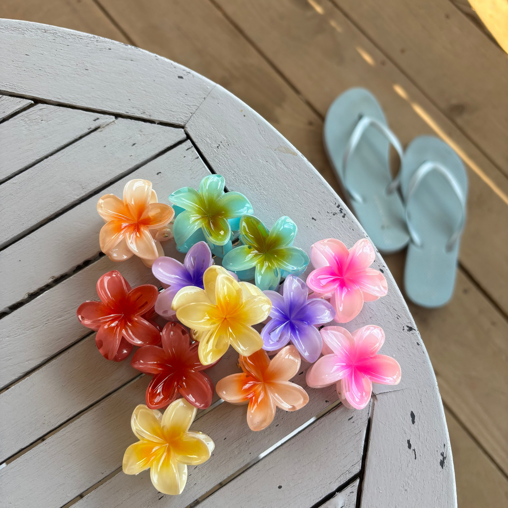 Colourful flower-shaped hair clips on a wooden surface with light blue flip-flops in the background.