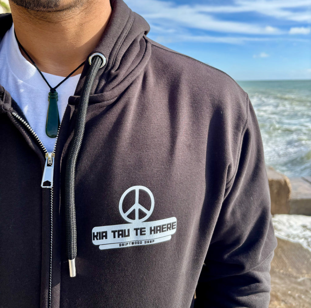 Person wearing a hoodie with a peace symbol and text by the ocean