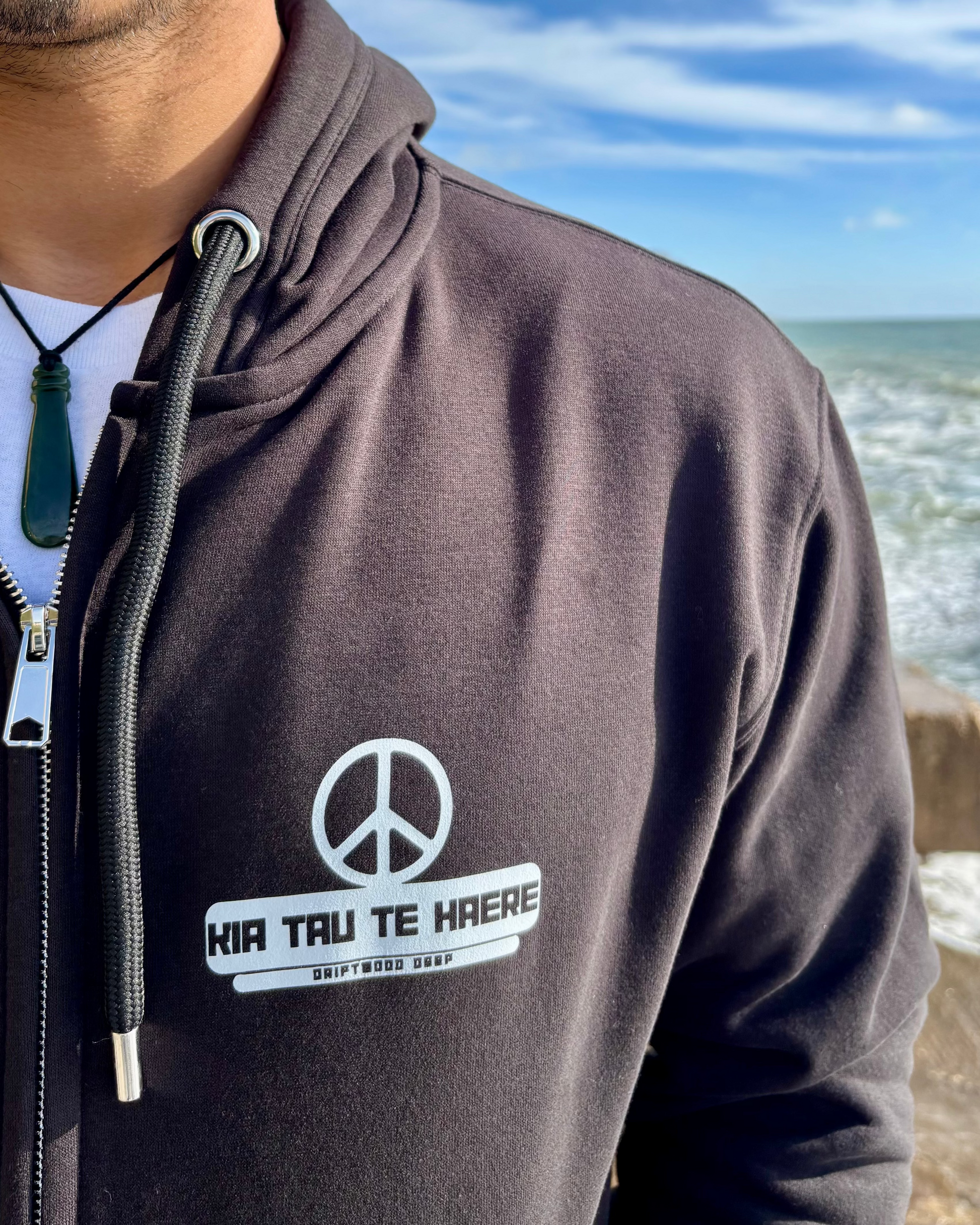 Person wearing a hoodie with a peace symbol and text by the ocean
