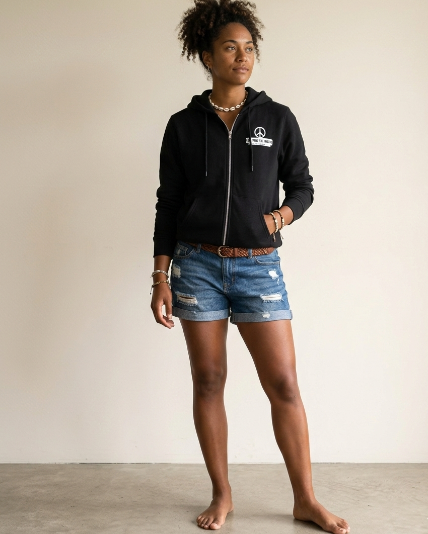Person wearing a black hoodie with a logo and denim shorts on a plain background