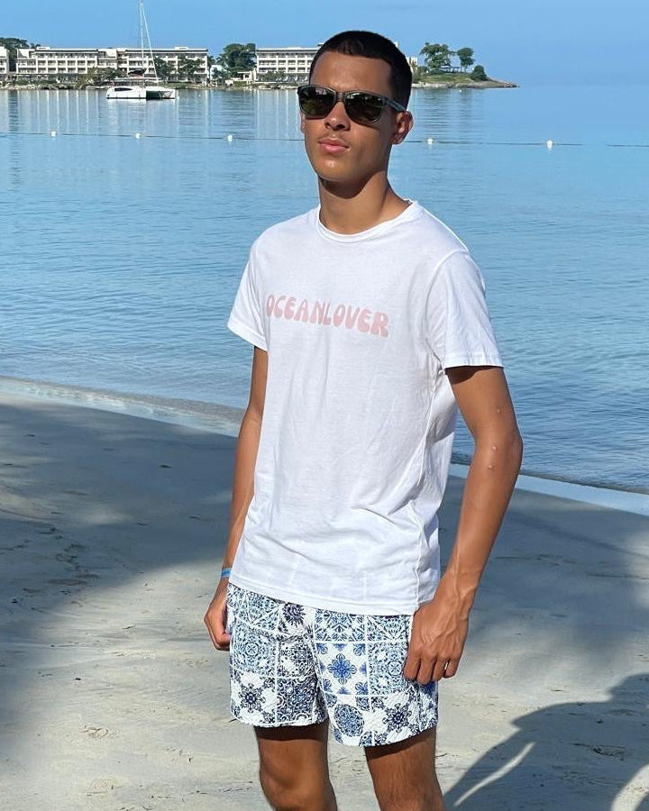 Person standing on a beach wearing sunglasses, a white t-shirt, and patterned shorts.