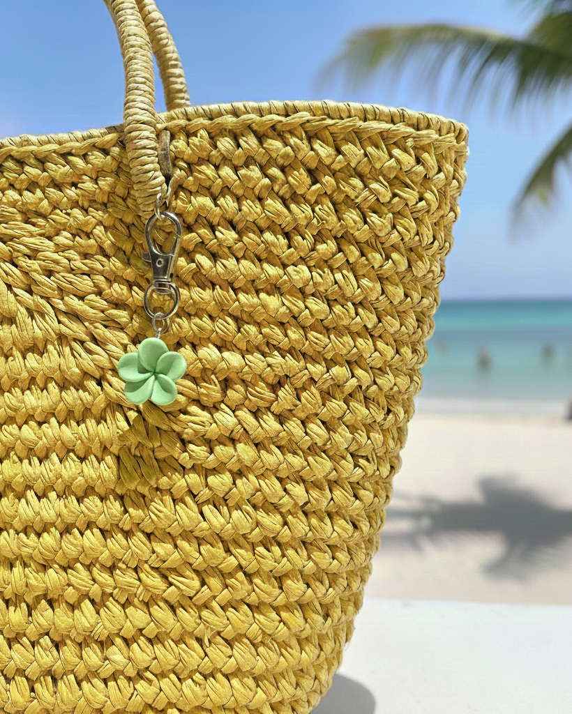 Yellow woven bag with a green flower charm on a beach background
