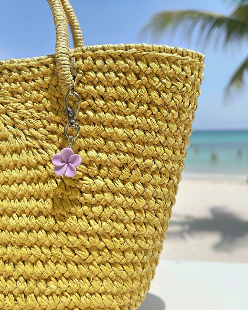 Yellow woven bag with a purple flower charm on a beach background
