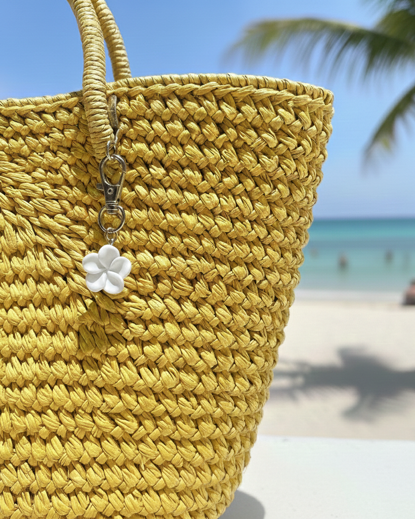 Yellow woven bag with a white flower charm on a beach background