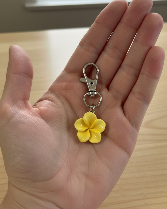 Yellow flower keychain held in a hand on a wooden surface