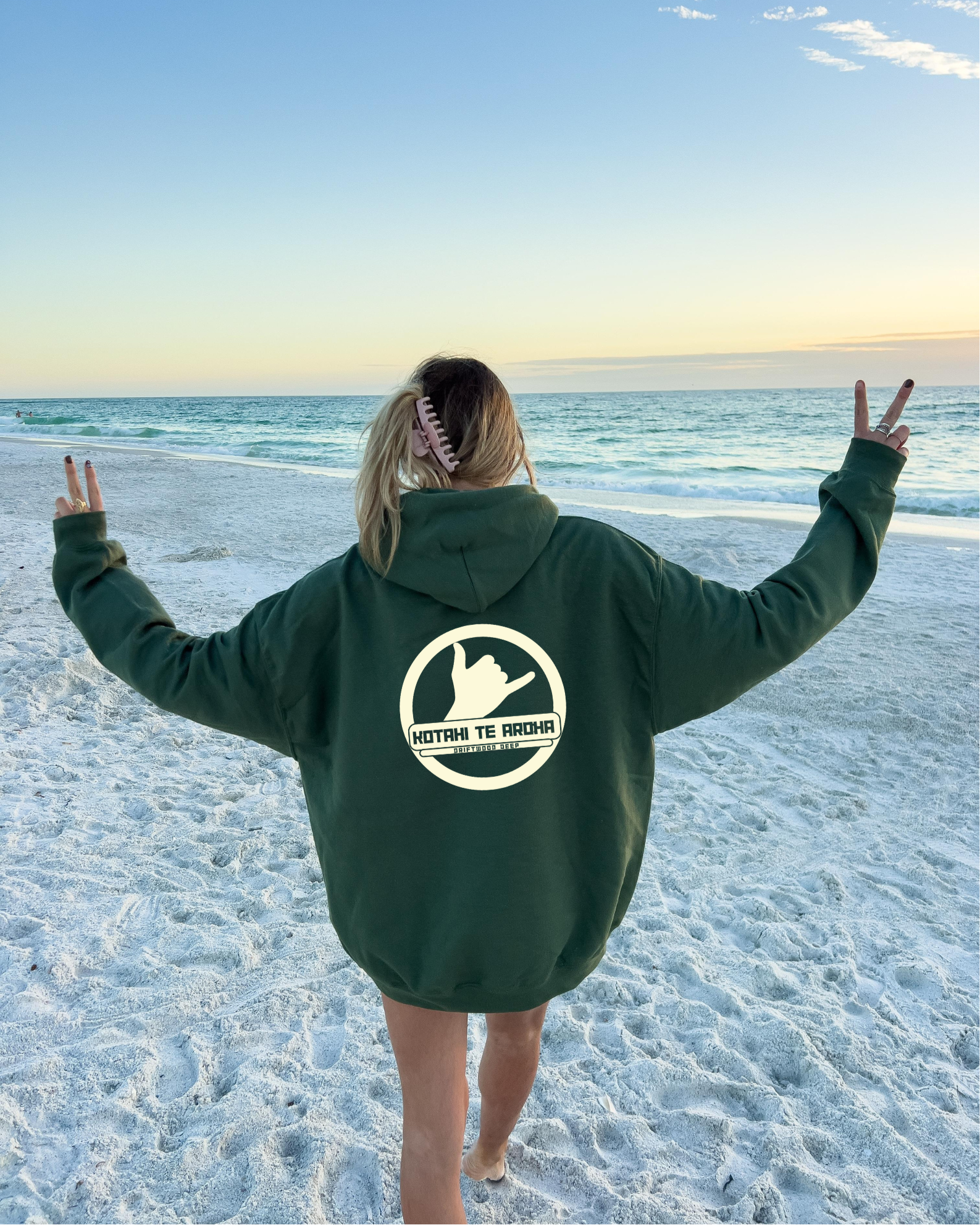 Person wearing a green hoodie with a logo on the beach