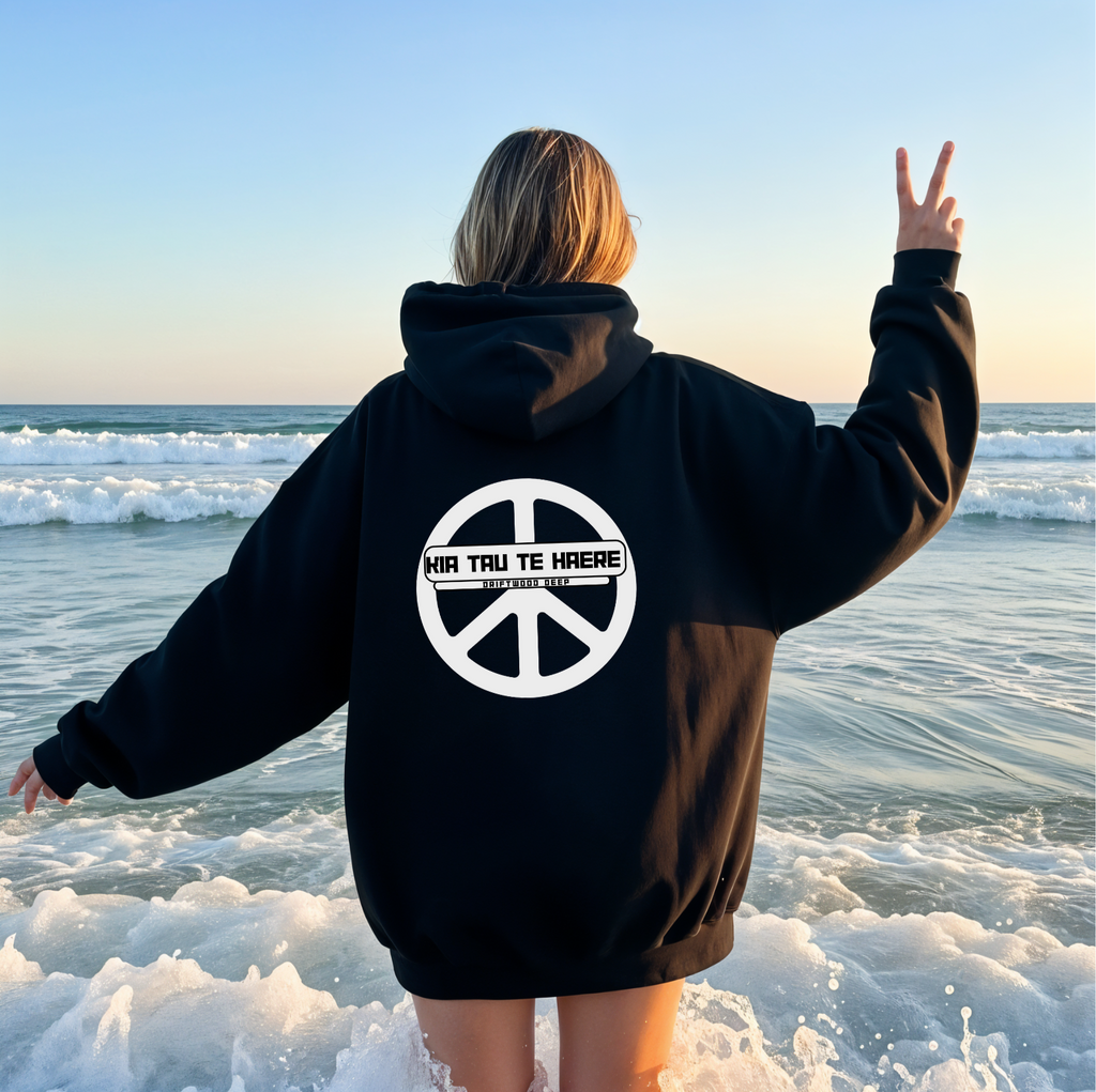 Person wearing a black hoodie with a peace symbol and text on the beach