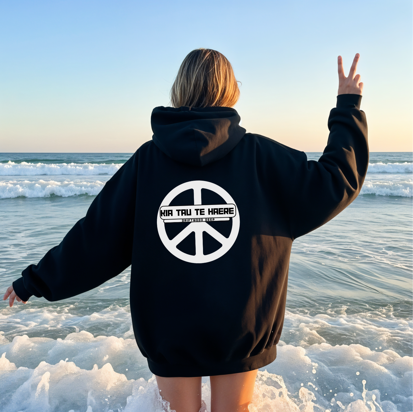 Person wearing a black hoodie with a peace symbol and text on the beach
