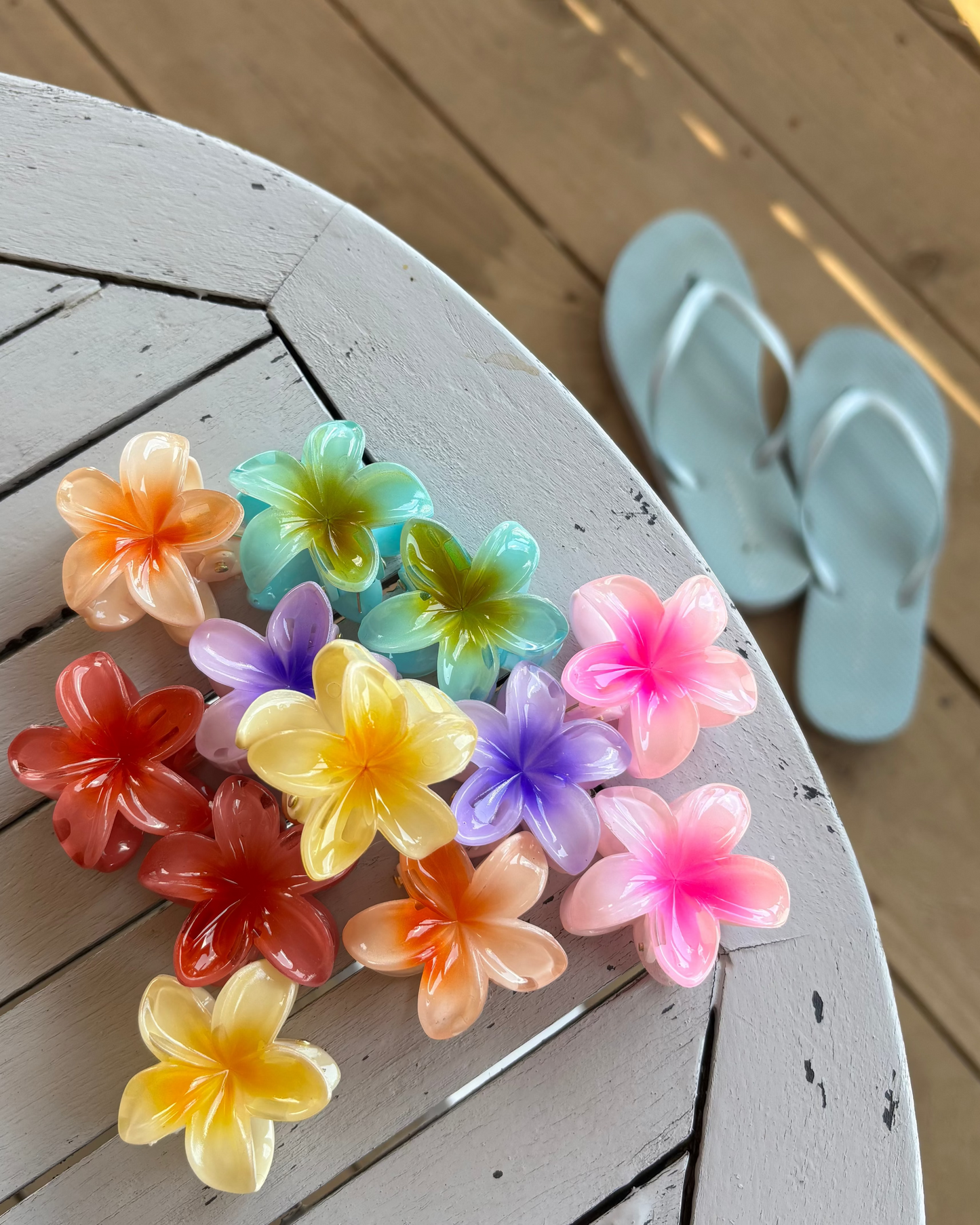 Colourful flower-shaped hair clips on a wooden surface with light blue flip-flops in the background.