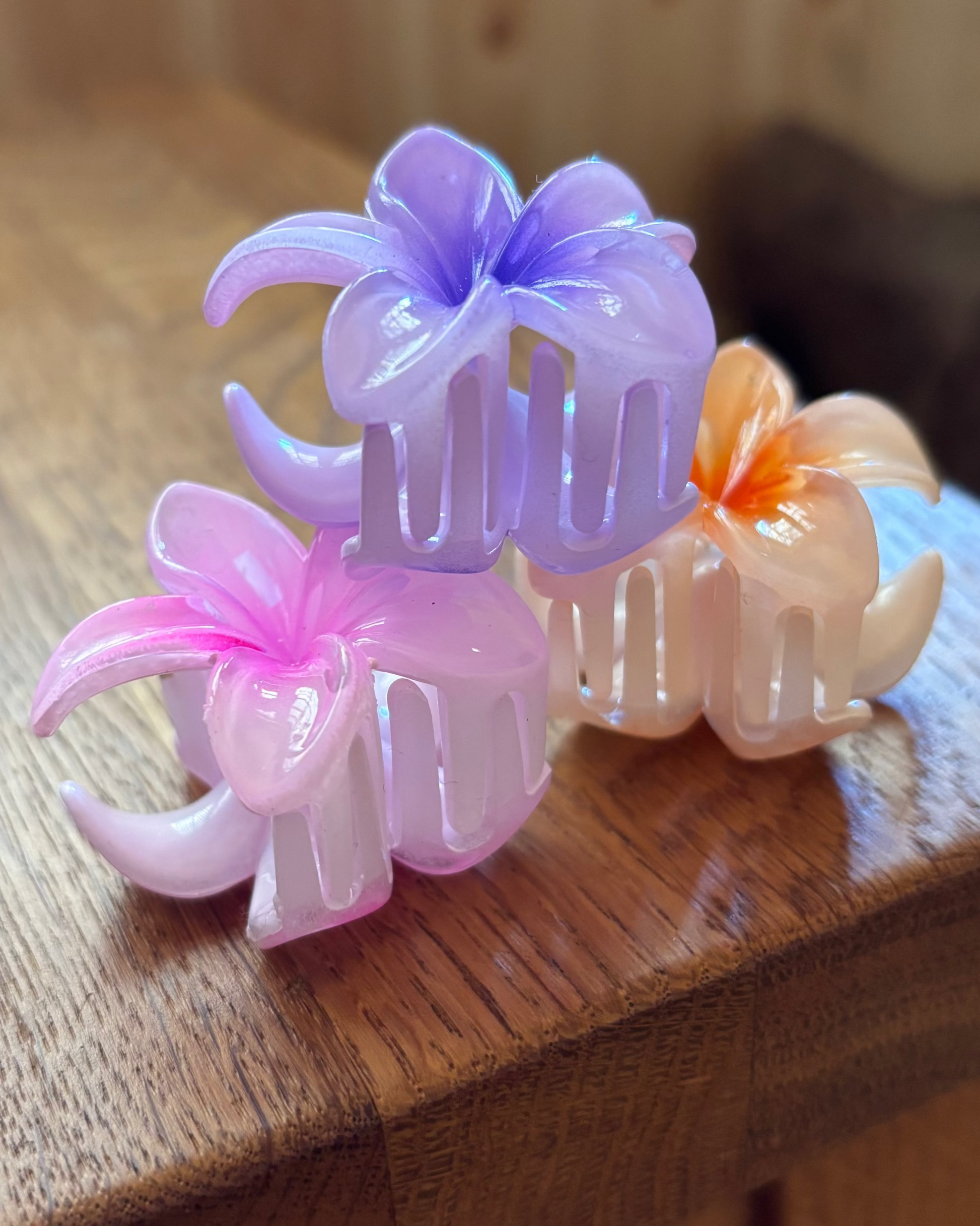 Three floral-shaped hair clips in pink, purple, and orange on a wooden surface.