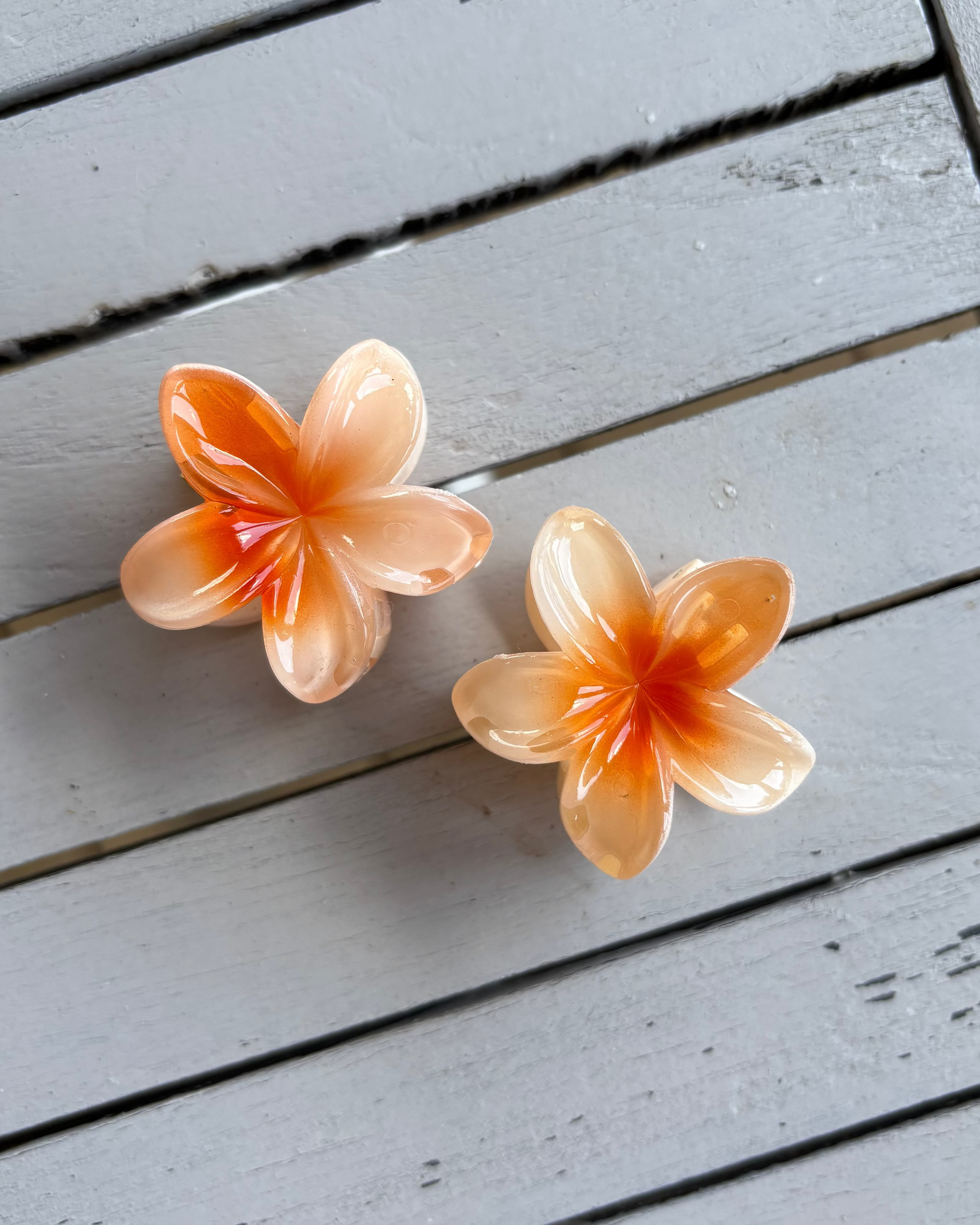 Two peach-colored flower-shaped hair clips on a wooden surface