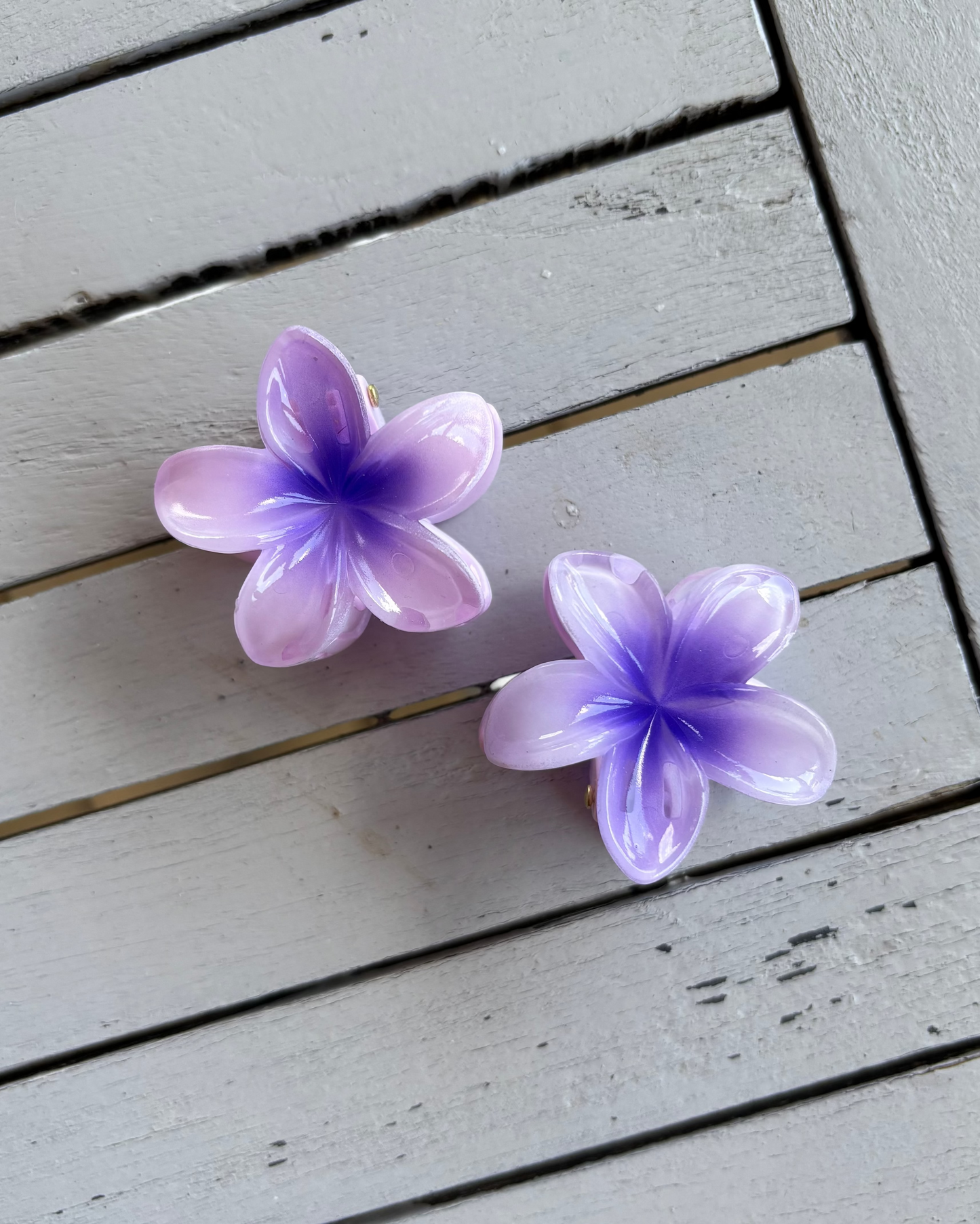 Two purple flower-shaped hair clips on a wooden surface